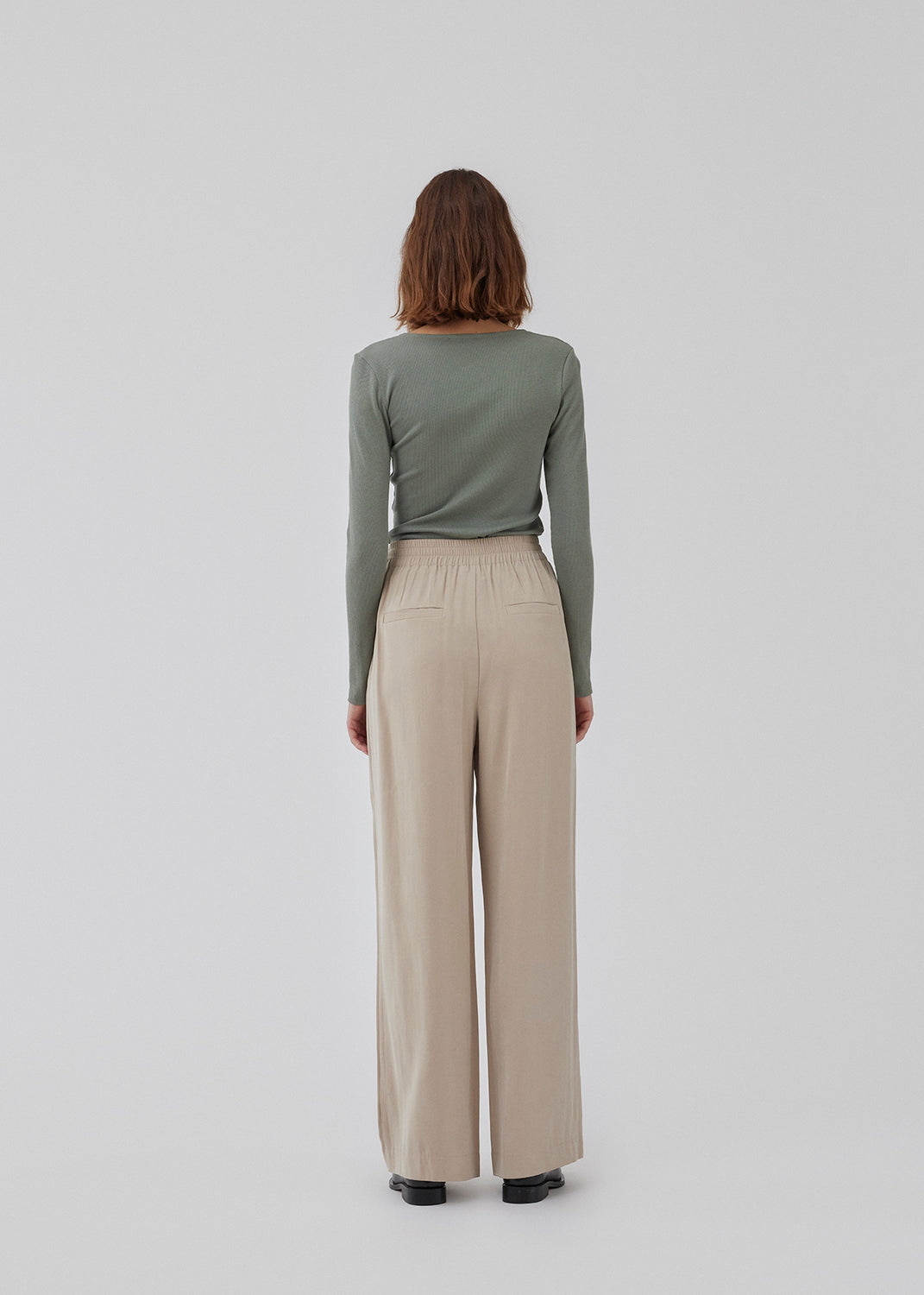 FanyaMD pants in bright beige have a menswear-inspired look with straight, wide legs, a high waist with zip fly and button and elastication in back. Doubble pleat in front and side pockets. The model is 175 cm and wears a size S/36.