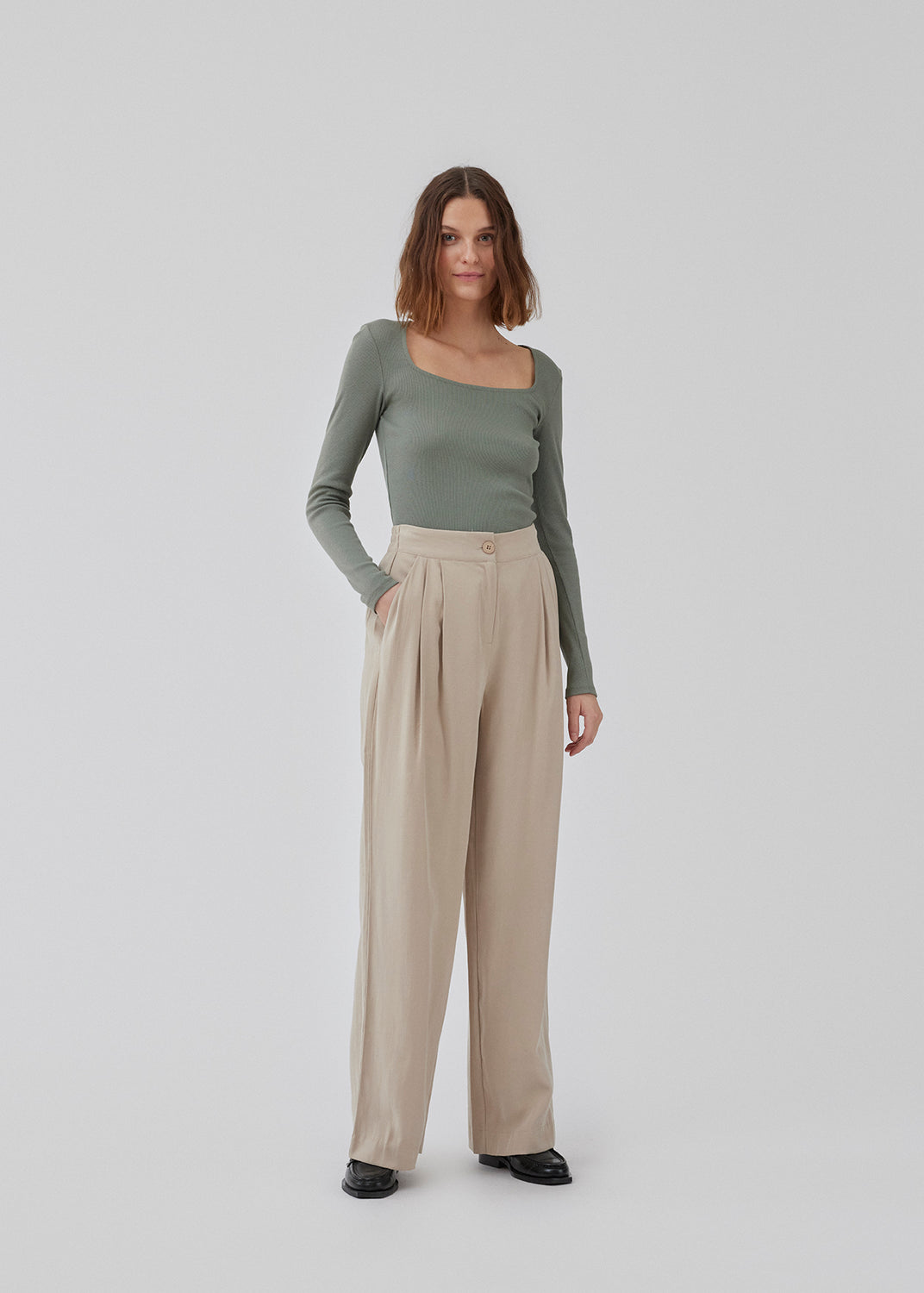 FanyaMD pants in bright beige have a menswear-inspired look with straight, wide legs, a high waist with zip fly and button and elastication in back. Doubble pleat in front and side pockets. The model is 175 cm and wears a size S/36.