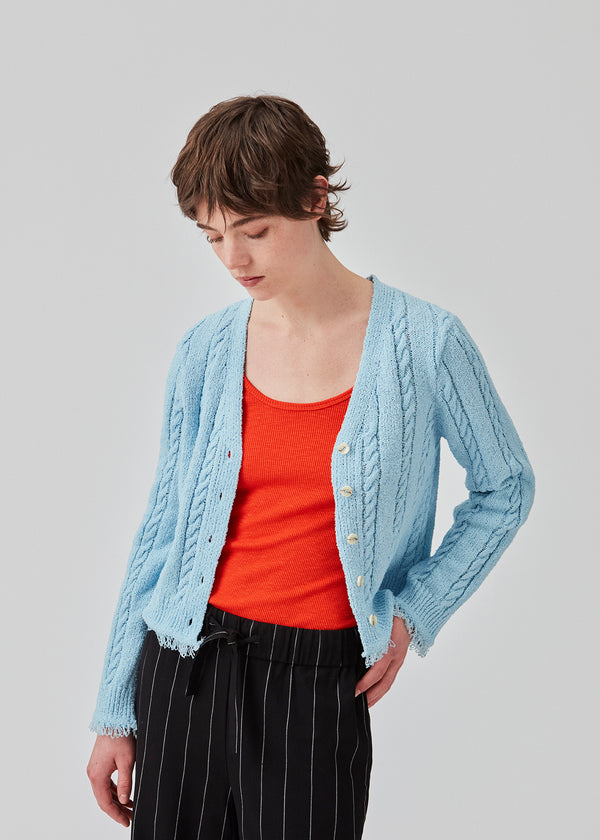 Light blue cardigan in cotton cable knit. Oversized and slightly cropped shape with long sleeves and raw trimmings. FinaMD cardigan has a v-neckline and buttons in front. The model is 175 cm and wears a size S/36.