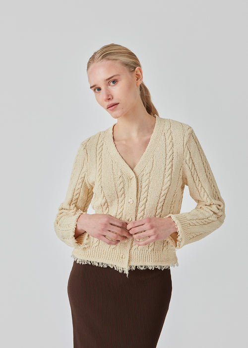 Beige cardigan in cotton cable knit. Oversized and slightly cropped shape with long sleeves and raw trimmings. FinaMD cardigan has a v-neckline and buttons in front. The model is 175 cm and wears a size S/36.