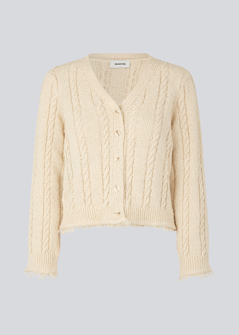 Beige cardigan in cotton cable knit. Oversized and slightly cropped shape with long sleeves and raw trimmings. FinaMD cardigan has a v-neckline and buttons in front. The model is 175 cm and wears a size S/36.
