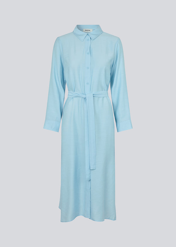 Midi dress in baby blue in woven quality with collar, buttons in front, detachable tie belt at the waist and a slit at each side. Long sleeves with cuff. The model is 175 cm and wears a size S/36.