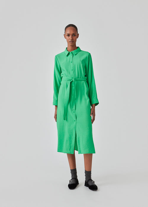 Midi dress in green in woven quality with collar, buttons in front, detachable tie belt at the waist and a slit at each side. Long sleeves with cuff. The model is 175 cm and wears a size S/36.
