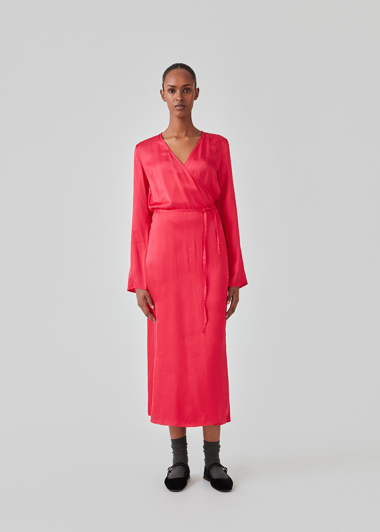 Long dress in pink in a satin-woven EcoVero viscose blend. FloreMD wrap dress has a v-neckline and wrap detail with a thin tie belt. Long sleeves with a slit at the hem. The model is 175 cm and wears a size S/36.