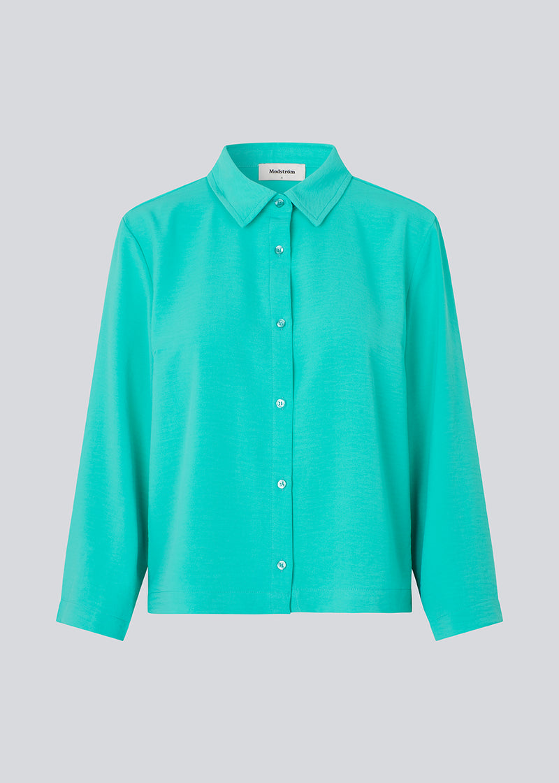 Cropped shirt in turquoise with a flowy and relaxed fit. FredaMD shirt has a collar and button closure in front, along with 3/4 length wide sleeves. The model is 175 cm and wears a size S/