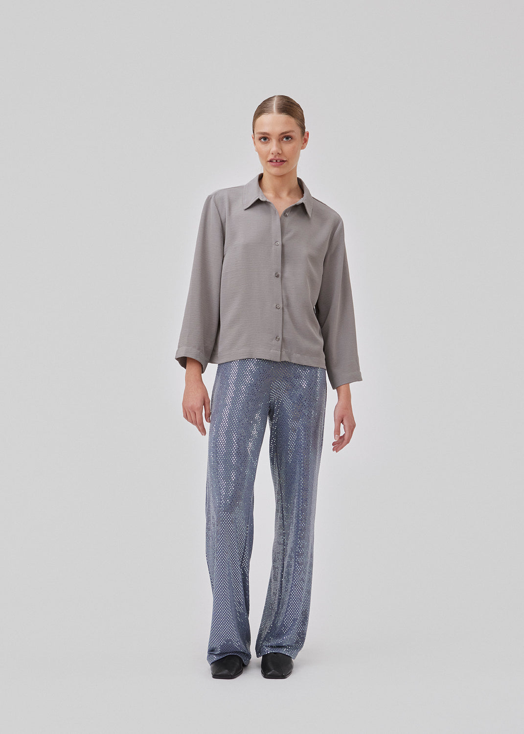 Cropped grey shirt with a flowy and relaxed fit. FredaMD shirt has a collar and button closure in front, along with 3/4 length wide sleeves. The model is 175 cm and wears a size S/36.