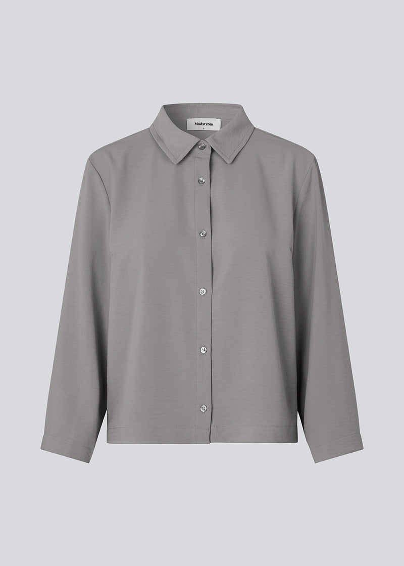 Cropped grey shirt with a flowy and relaxed fit. FredaMD shirt has a collar and button closure in front, along with 3/4 length wide sleeves. The model is 175 cm and wears a size S/36.