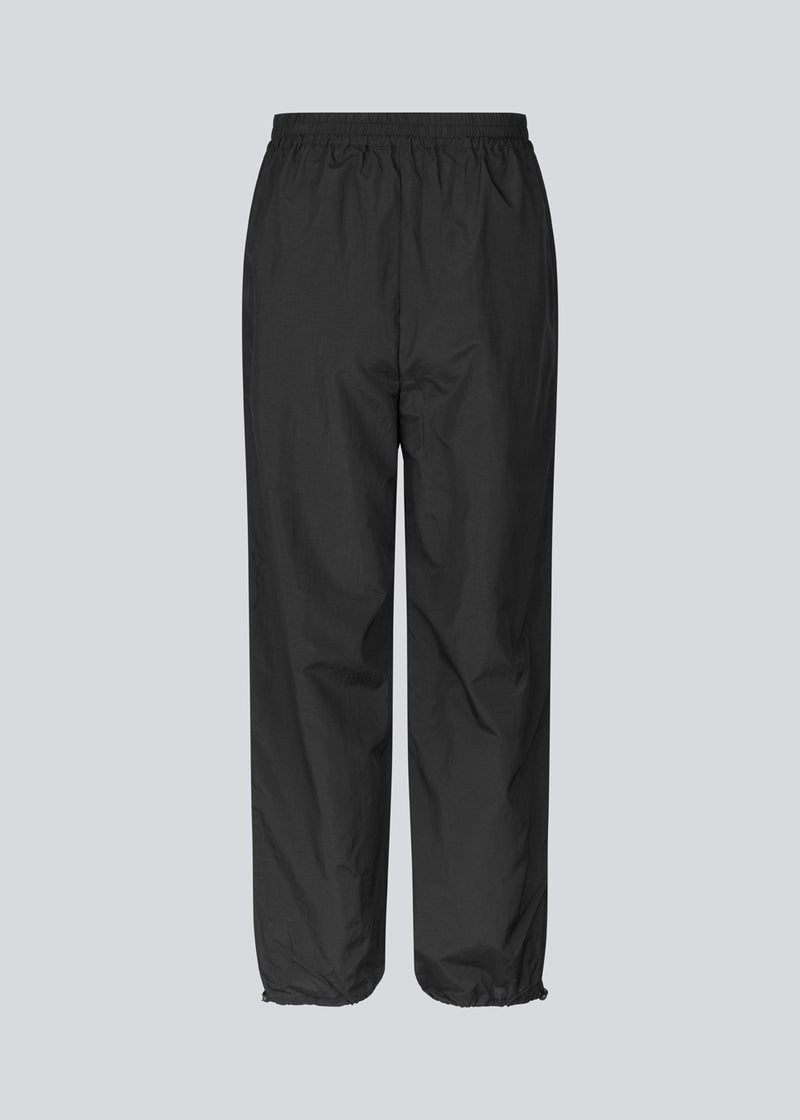 Parachute black pants in nylon with a relaxed fit. FumikoMD pants have a regular waist with elastic, wide legs and elastic drawstring at the waist. 