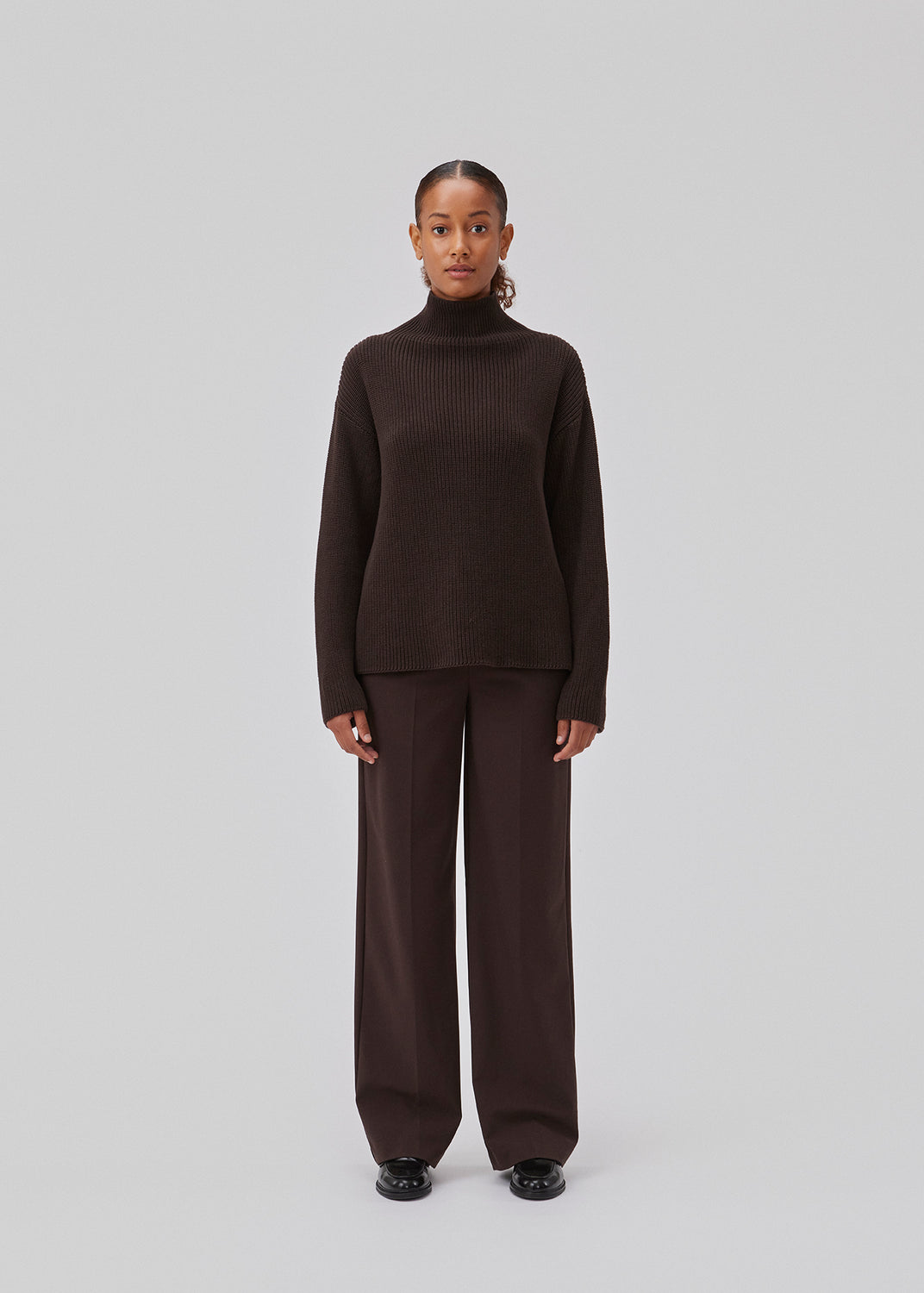 GalenMD t-neck in brown knitted from organic cotton with an oversized shape, lange and wide sleeves, along with a high neck and dropped shoulders. The model is 175 cm and wears a size S/36.