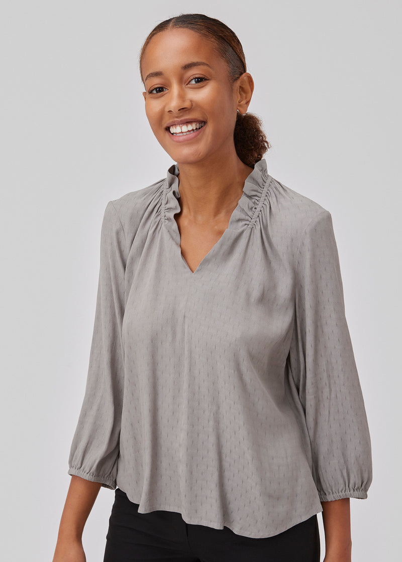 Top in grey with a relaxed fit. GilliganMD top has a v-shaped neckline with ruching around the neck and 3/4 length balloon sleeves with elastics at cuff. The model is 175 cm and wears a size S/36.