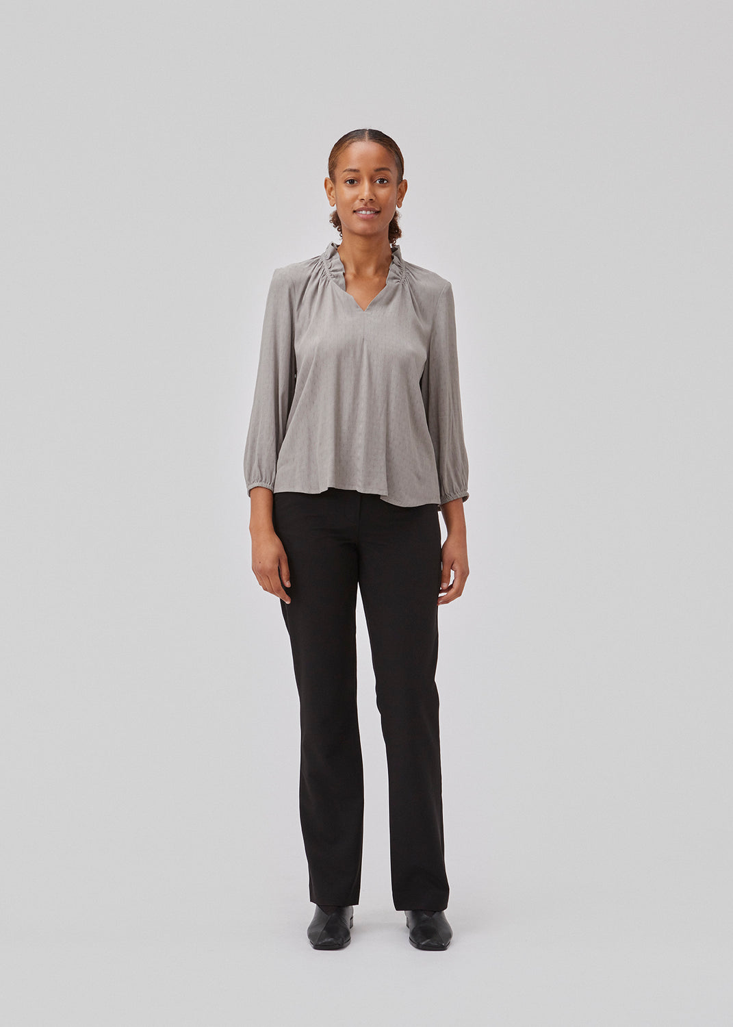 Top in grey with a relaxed fit. GilliganMD top has a v-shaped neckline with ruching around the neck and 3/4 length balloon sleeves with elastics at cuff. The model is 175 cm and wears a size S/36.