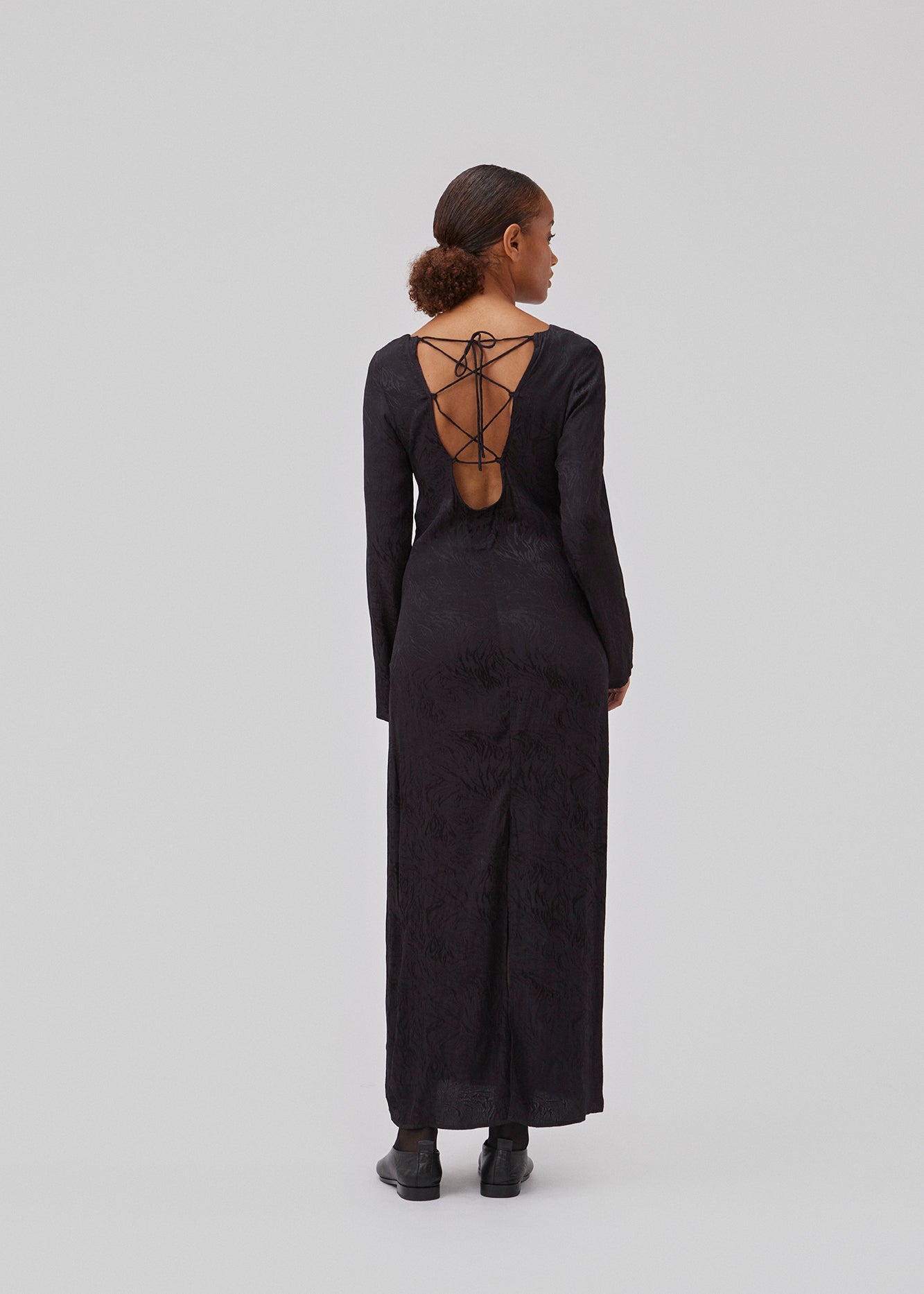 Long sleeved dress in jacquard satin. GraceyMD dress is designed with a relaxed fit and a deep opening in the back with lacing and narrow ties. Slit at center back. The model is 175 cm and wears a size S/36.