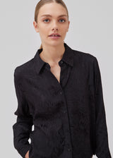 Shirt in black in jacquard satin in a slightly cropped length. GraceyMD shirt has a loose fit with long sleeves, cuff, collar and buttons in front. The model is 175 cm and wears a size S/36.