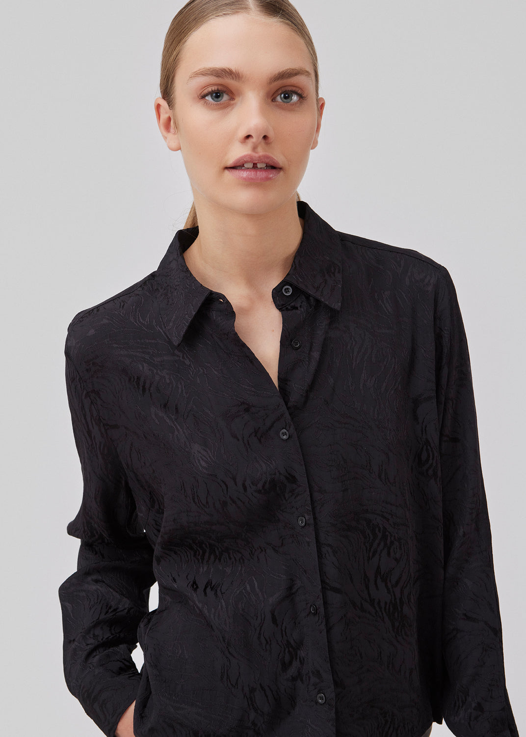 Shirt in black in jacquard satin in a slightly cropped length. GraceyMD shirt has a loose fit with long sleeves, cuff, collar and buttons in front. The model is 175 cm and wears a size S/36.