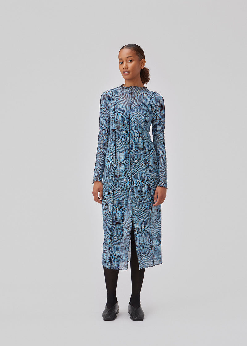 Mesh dress with a high neck, long sleeves and midi length. GwenMD print dress has decorative lettuce hems on the body, neck and sleeves. The dress has a slit in front and is slightly transparent. The model is 175 cm and wears a size S/36.