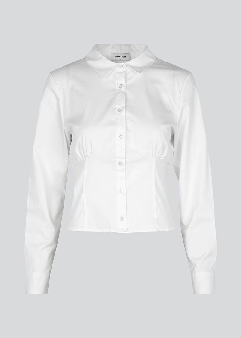 Form-fitting shirt in white in a woven cotton blend with collar, buttons in front, and long sleeves with cuff. HarrisonMD shirt has darts and a cutline below the chest for a corset-inspired look. The model is 175 cm and wears a size S/36.