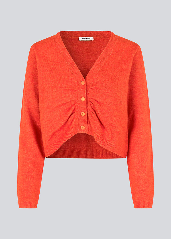 Cropped cardigan in bright red in a soft material. HeatMD cardigan has a v-neckline and button closure in front with ruching. The sleeves are long. 
