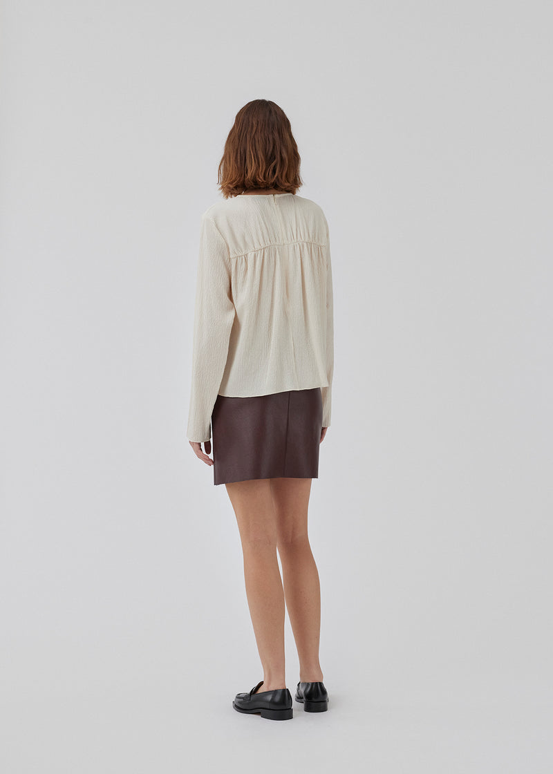 HiltonMD top in beige is designed with a relaxed fit, long sleeves and a round neckline with a hidden zipper at the back. The top is detailed with a ruching detail over the chest. The model is 175 cm and wears a size S/36.