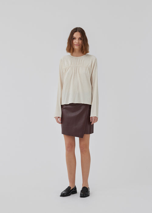 HiltonMD top in beige is designed with a relaxed fit, long sleeves and a round neckline with a hidden zipper at the back. The top is detailed with a ruching detail over the chest. The model is 175 cm and wears a size S/36.