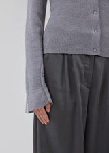 Fitted cardigan in grey melange made from a soft, rib-knitted wool. HirokiMD cardigan has a collar, buttons in front, and long sleeves with slit and buttons. The model is 175 cm and wears a size S/36.