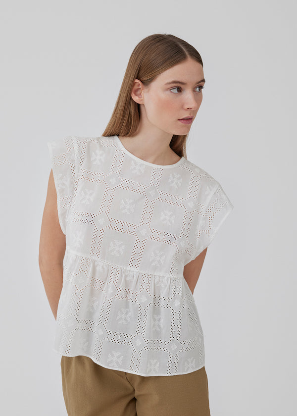 Top in white in broderie anglaise cotton with cutline below the chest with extra volume. HollynMD top has a round neck, short sleeves, and a small opening at the neck with button closure. The model is 175 cm and wears a size S/36.