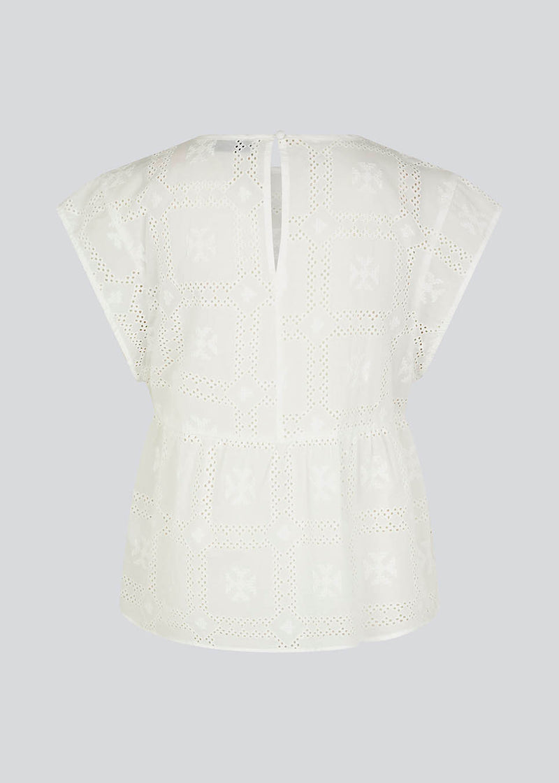Top in white in broderie anglaise cotton with cutline below the chest with extra volume. HollynMD top has a round neck, short sleeves, and a small opening at the neck with button closure. The model is 175 cm and wears a size S/36.