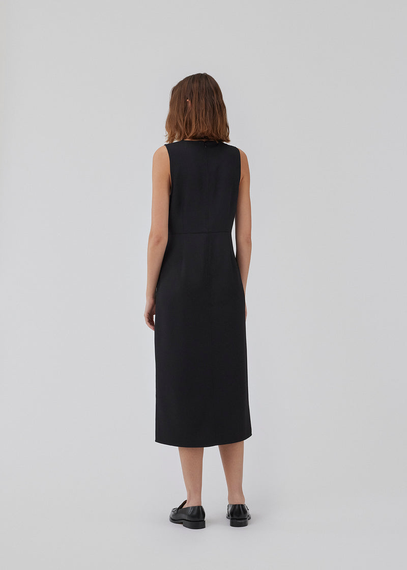 Dress in black with a slim silhouette, round neck, and without sleeves. HomerMD dress has an elegant look with a cutline mid front and back, and a high slit in front. Hidden zipper in the back. The model is 175 cm and wears a size S/36.