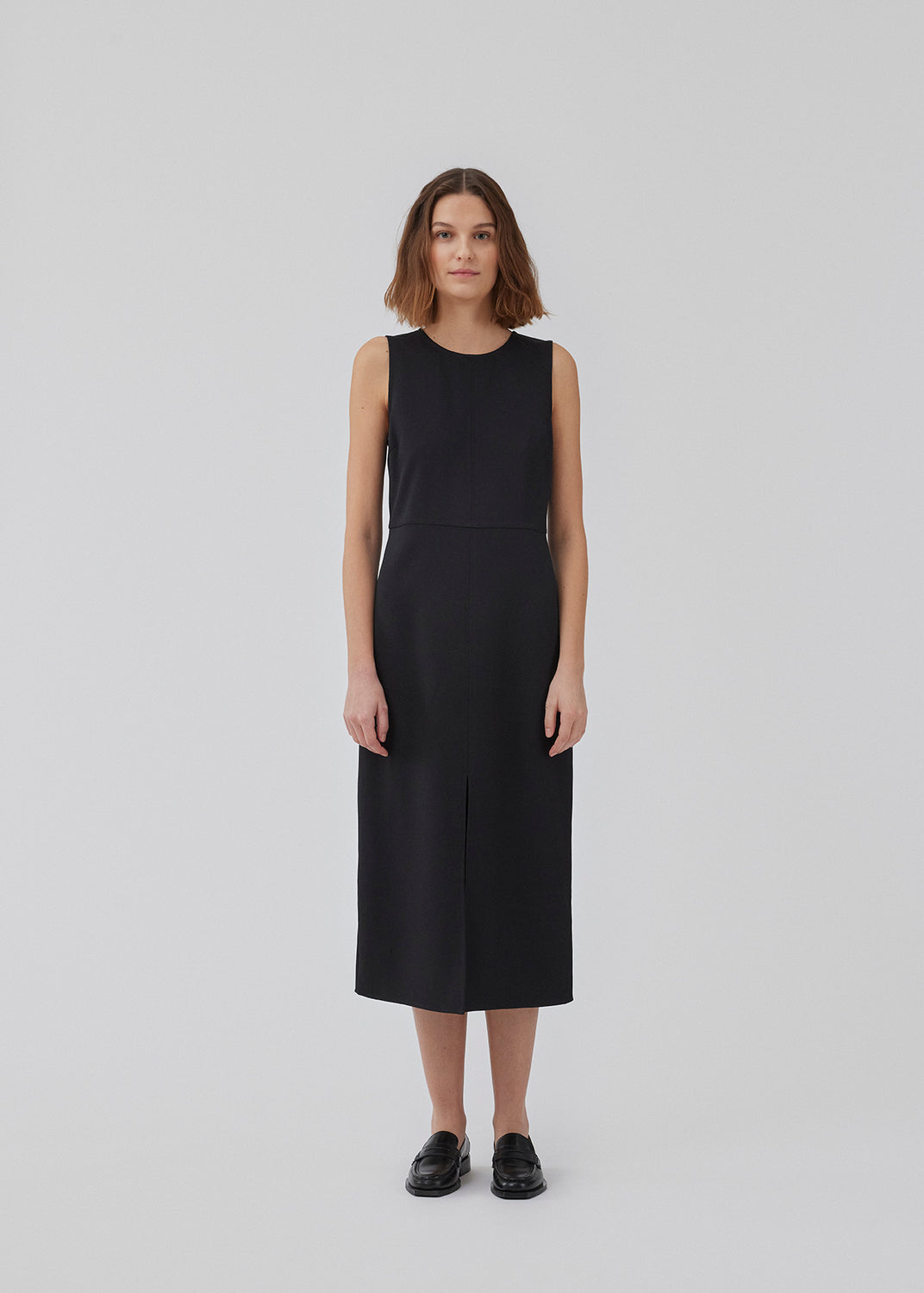 Dress in black with a slim silhouette, round neck, and without sleeves. HomerMD dress has an elegant look with a cutline mid front and back, and a high slit in front. Hidden zipper in the back. The model is 175 cm and wears a size S/36.