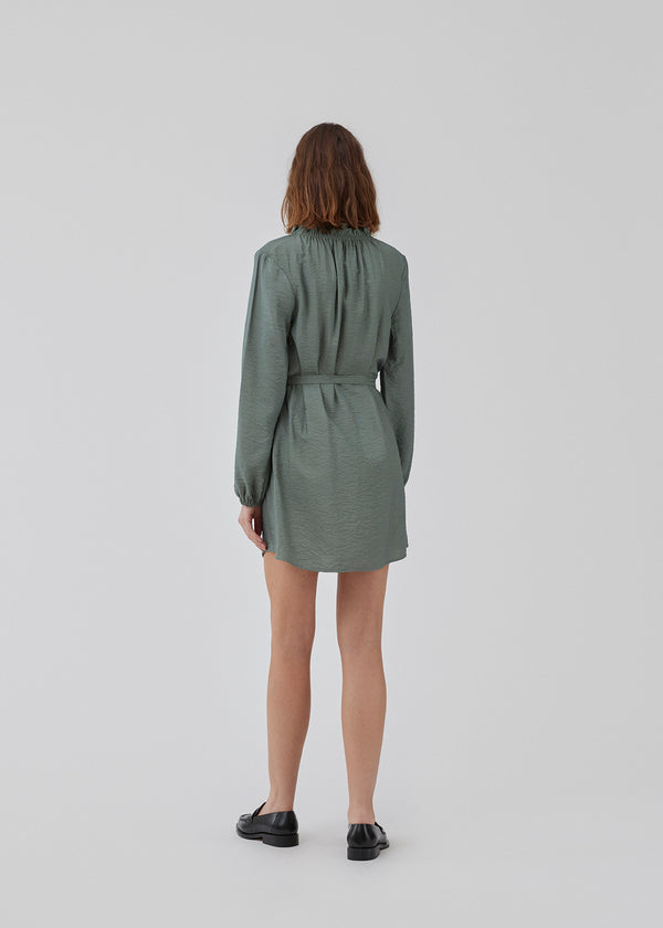 Short dress with long sleeves and a loose silhouette. HudgesMD dress has a v-shaped neckline with ruffles and a tiebelt at the waist. The model is 175 cm and wears a size S/36.