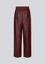 Pants in faux leather in burgundy with wide legs and a high, elasticated waist. HuxleyMD pants has side pockets, decorative fly, and a raw bottom edge. The model is 175 cm and wears a size S/36.