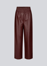 Pants in faux leather in burgundy with wide legs and a high, elasticated waist. HuxleyMD pants has side pockets, decorative fly, and a raw bottom edge. The model is 175 cm and wears a size S/36.