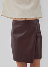 Short, asymmetrical wrap skirt in Burgundy in faux leather. HuxleyMD skirt has a hidden zipper closure at one side. The model is 175 cm and wears a size S/36.