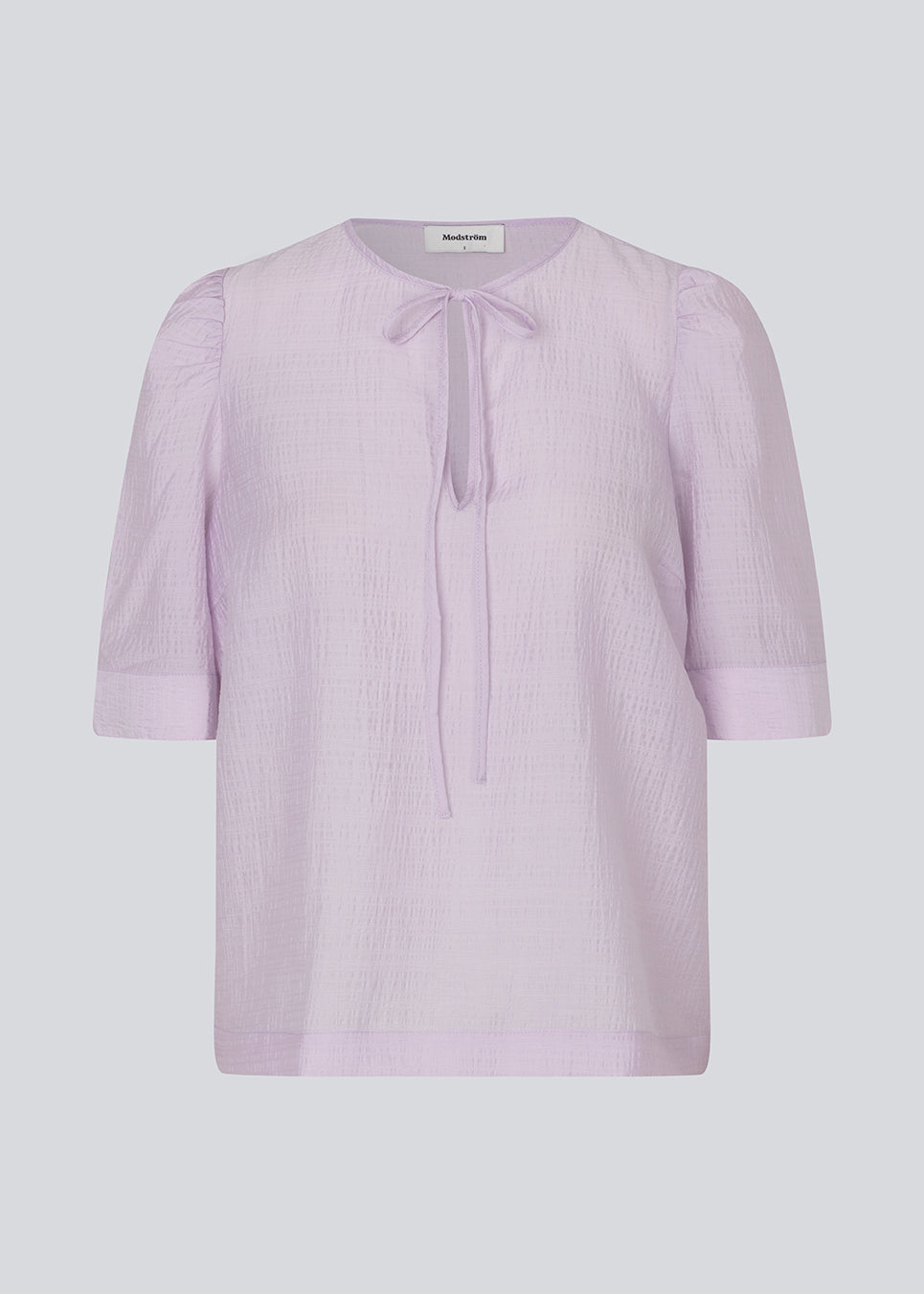 Loose top in light purple with short puff sleeves with a button closing. IbiMD top has an opening in the front with a tieband.