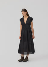 Sleeveless black maxi dress with a loose fit. IndiaMD dress has a deep v-neckline and a tie band at the waist and under the chest. The model is 177 cm and wears a size S/36.