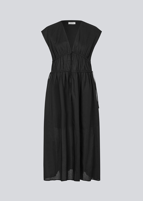 Sleeveless black maxi dress with a loose fit. IndiaMD dress has a deep v-neckline and a tie band at the waist and under the chest. The model is 177 cm and wears a size S/36.