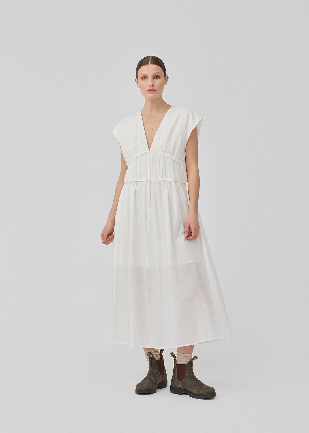 Sleeveless white maxi dress with a loose fit. IndiaMD dress has a deep v-neckline and a tie band at the waist and under the chest. The model is 177 cm and wears a size S/36.