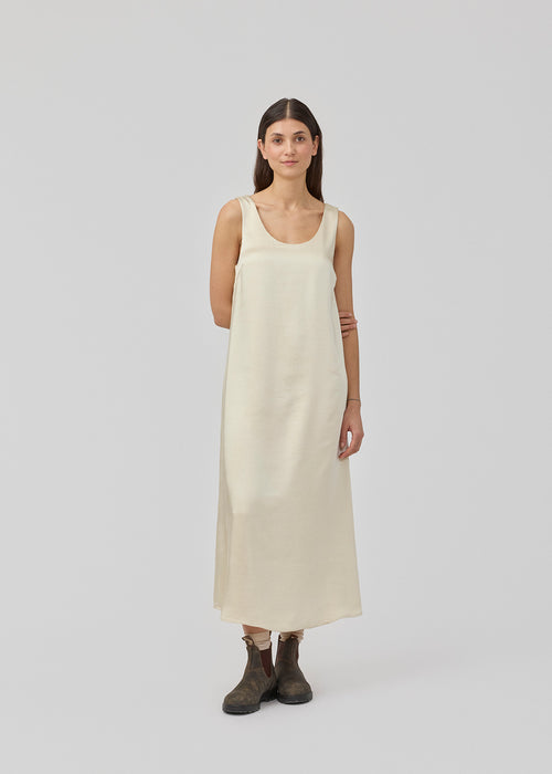 Long dress in beige in satin with an A-line silhouette. IolaMD dress has a deep back neckline and wide straps. The model is 177 cm and wears a size S/36.