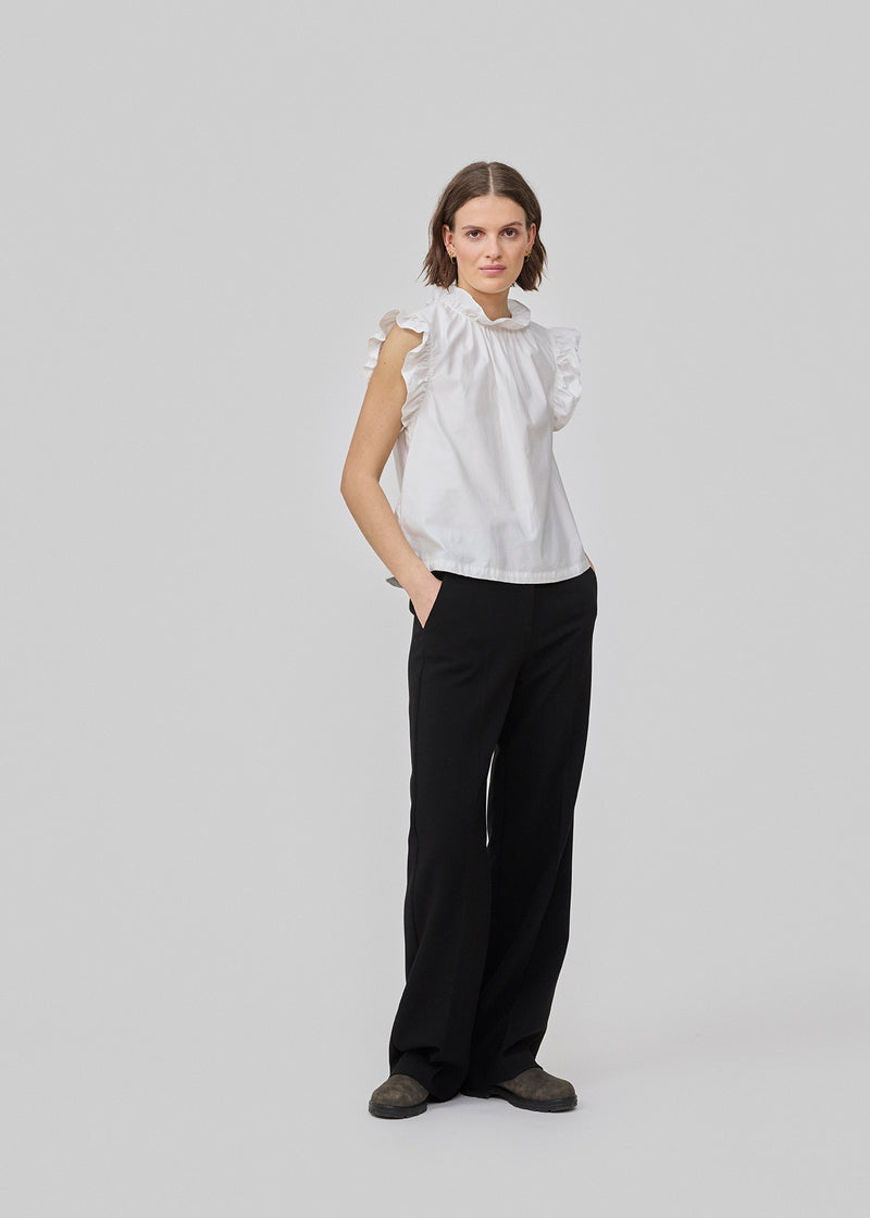 Loose white top with a ruffle detail at the sleeves and neck. IzakMD top is sleeveless and has a hidden zipper in the back. The model is 177 cm and wears a size S/36.