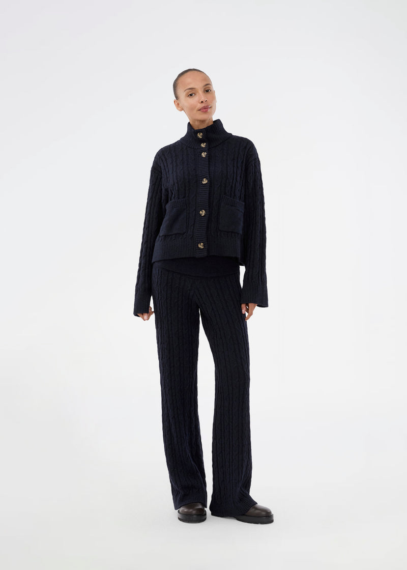 Josefine Vogt – high-neck cardigan. The Josefinemd knit cardigan features a cable-knit design with a high collar, buttoned cuffs, and front pockets. Timeless and perfect for chilly days, or as a layering piece over dresses and tops.