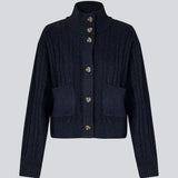 Josefine Vogt – high-neck cardigan. The Josefinemd knit cardigan features a cable-knit design with a high collar, buttoned cuffs, and front pockets. Timeless and perfect for chilly days, or as a layering piece over dresses and tops.