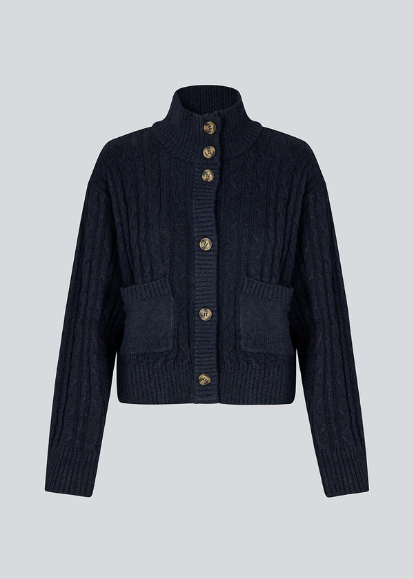 Josefine Vogt – high-neck cardigan. The Josefinemd knit cardigan features a cable-knit design with a high collar, buttoned cuffs, and front pockets. Timeless and perfect for chilly days, or as a layering piece over dresses and tops.