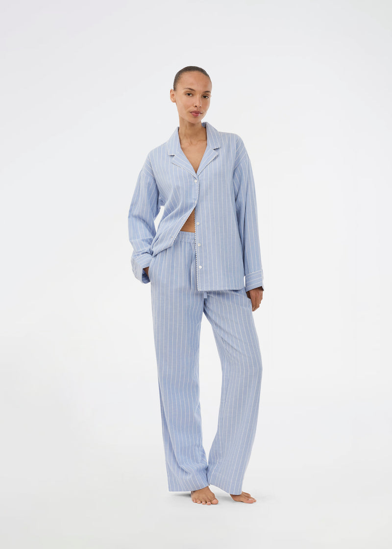 Blue classic striped pyjamas. The pyjamas is sold as a set of shirt and pants in the same size. Josefinemd pyjamas are made from 100% soft cotton and feature a classic fit with a collar, button closure, and drawstring trousers. Finished with delicate wave trim and comes with a matching pouch with logo. Josefine Vogt (165 cm) and the model (177 cm) are both wearing size Small.