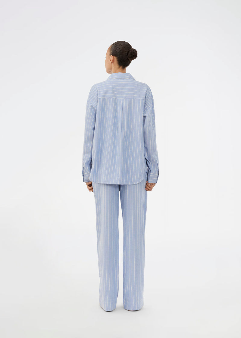 Blue classic striped pyjamas. The pyjamas is sold as a set of shirt and pants in the same size. Josefinemd pyjamas are made from 100% soft cotton and feature a classic fit with a collar, button closure, and drawstring trousers. Finished with delicate wave trim and comes with a matching pouch with logo. Josefine Vogt (165 cm) and the model (177 cm) are both wearing size Small.