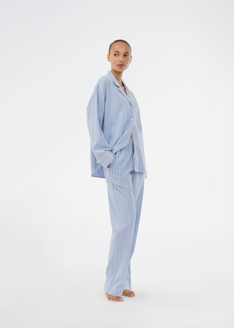 Blue classic striped pyjamas. The pyjamas is sold as a set of shirt and pants in the same size. Josefinemd pyjamas are made from 100% soft cotton and feature a classic fit with a collar, button closure, and drawstring trousers. Finished with delicate wave trim and comes with a matching pouch with logo. Josefine Vogt (165 cm) and the model (177 cm) are both wearing size Small.
