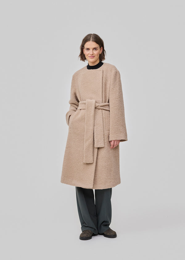 Long beige jacket with a loose fit and tieband. JustyMD jacket has a hidden button closure and a slit in the back and sidepockets.