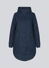 A warm water-repellent winter coat in navy blue with a high collar and hood. Keller coat has a hidden button and zipper closure at the front, along with zipped pockets. The coat has a relaxed silhouette with an adjustable elastic at the waist. The filling is a sustainable polyester padding with an extra high insulation ability.