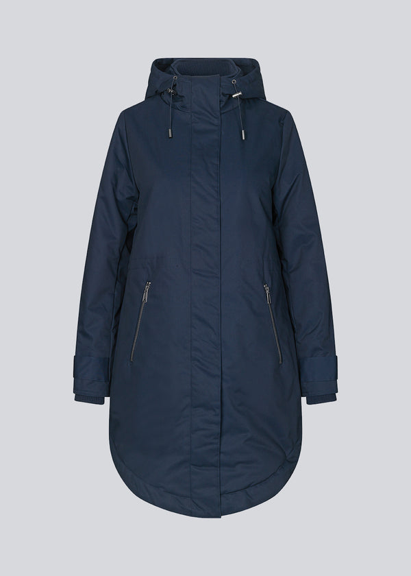 A warm water-repellent winter coat in navy blue with a high collar and hood. Keller coat has a hidden button and zipper closure at the front, along with zipped pockets. The coat has a relaxed silhouette with an adjustable elastic at the waist. The filling is a sustainable polyester padding with an extra high insulation ability.