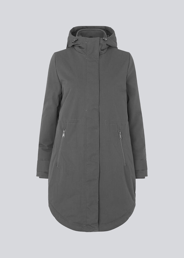 A warm water-repellent winter coat in grey with a high collar and hood. Keller coat has a hidden button and zipper closure at the front, along with zipped pockets. The coat has a relaxed silhouette with an adjustable elastic at the waist. The filling is a sustainable polyester padding with an extra high insulation ability.