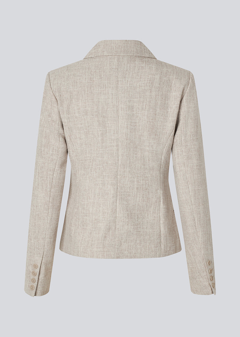 Short fitted blazer in beige melange in a structured material. KieraMD jacket has two pockets at the front and a slit at the sleeves with button closure.
