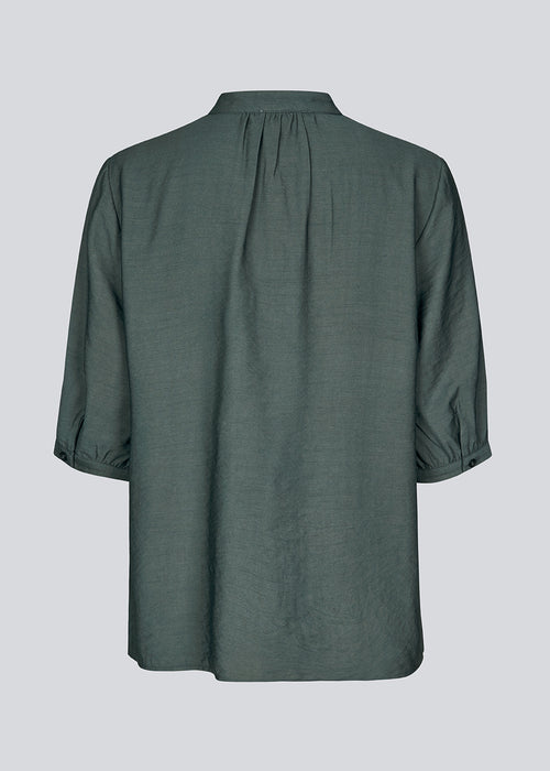 Loose shirt in dark green with short sleeves and a ruffel detail. KirisMD top has a button closure in front and puff sleeves.